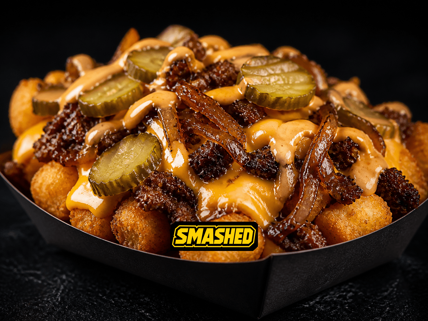 Loaded tots with chopped smash patty, cheese, onions, pickles, and sauce in a black SMASHED box